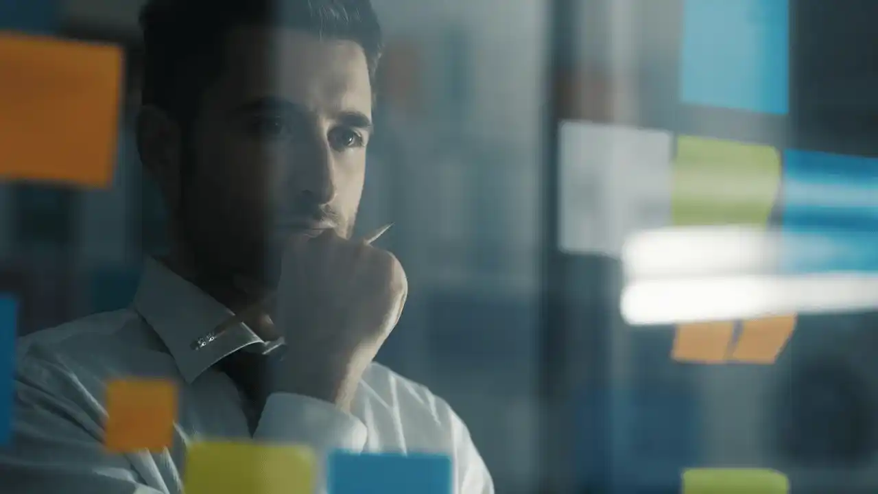 Profesional reflexionando frente a un tablero con notas adhesivas durante la planificación estratégica.